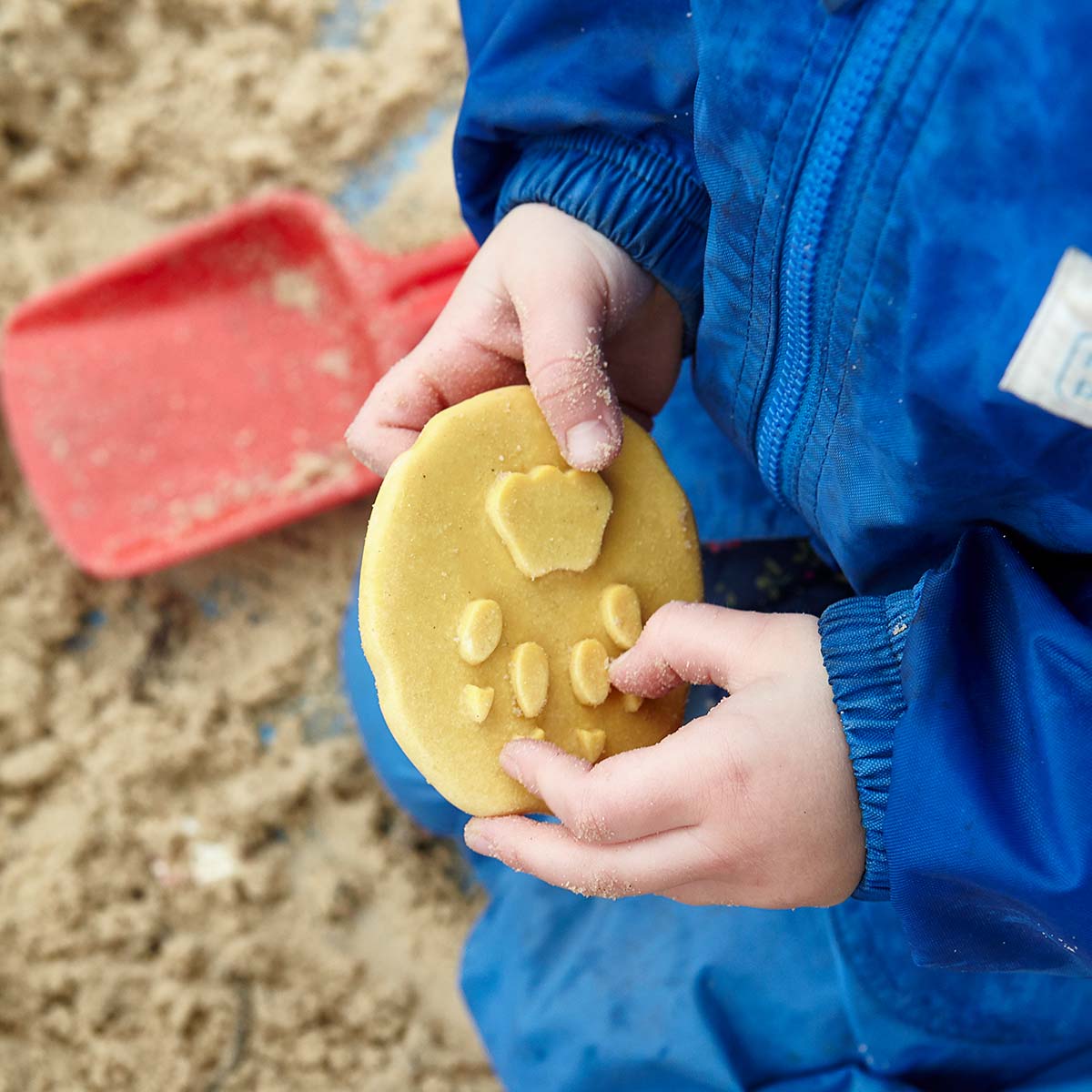 dieťa v modrej bunde na pieskovisku drží v ruke hnedú kamennú stopu geparda