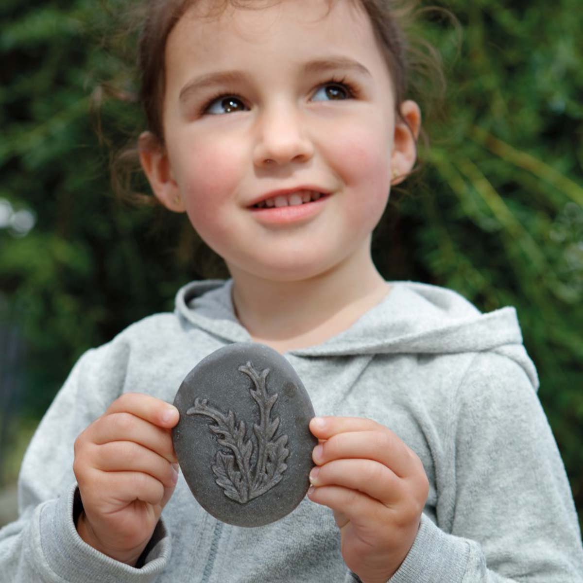 malé dievča drží v rukách sivý kamenný odliatok morskej riasy